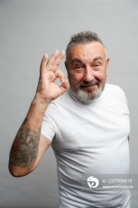 Portrait of senior man showing OK sign against gray background