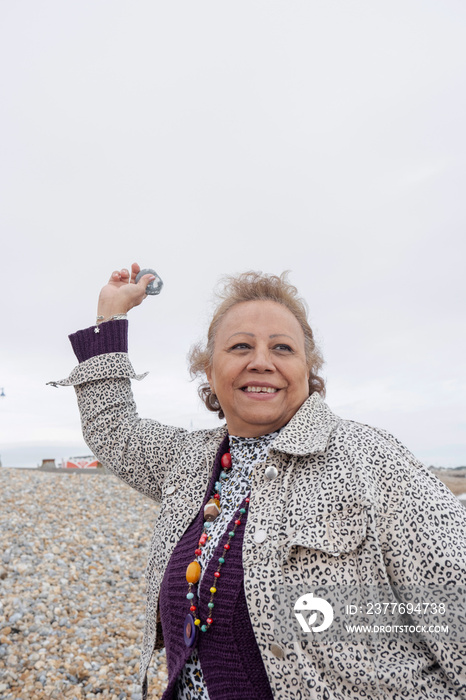 Smiling senior woman skimming stones on beach