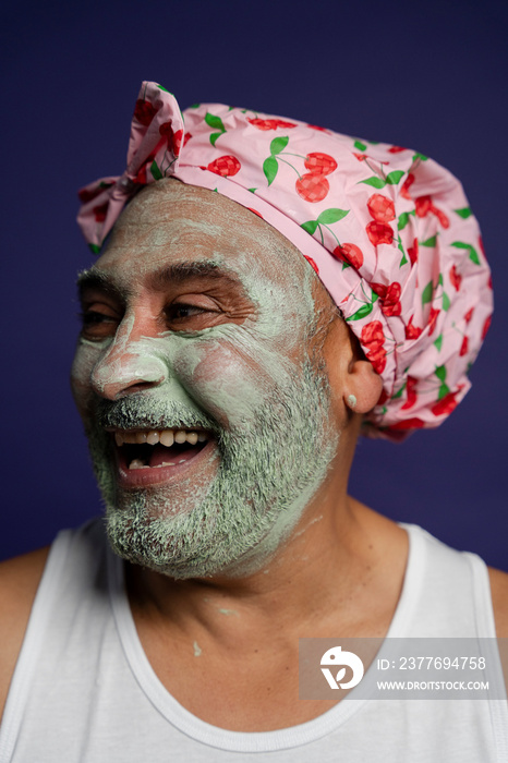 Portrait of man in facial mask and hair cap against purple background