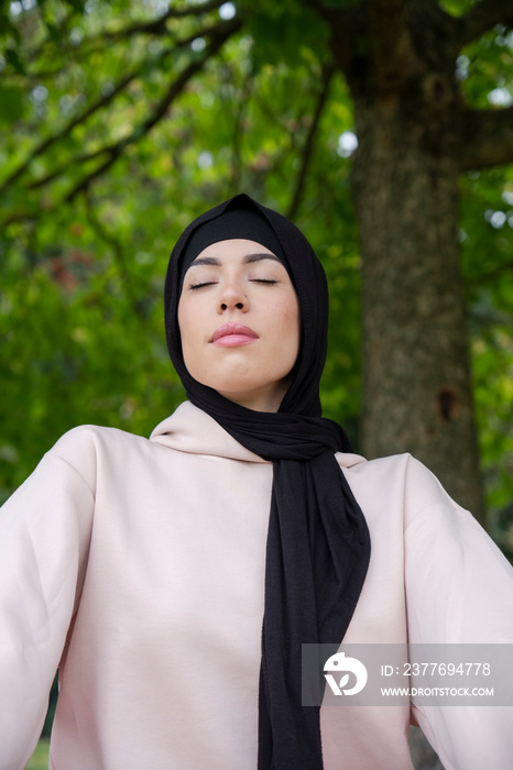 Portrait of woman in hijab and pink tracksuit meditating in park