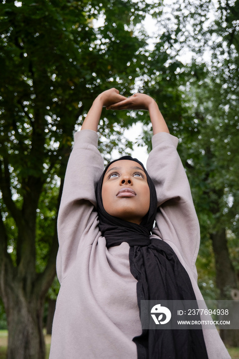 Portrait of woman in hijab stretching in park