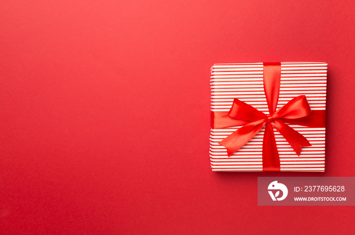 Gift box with red ribbon bow on color background, top view