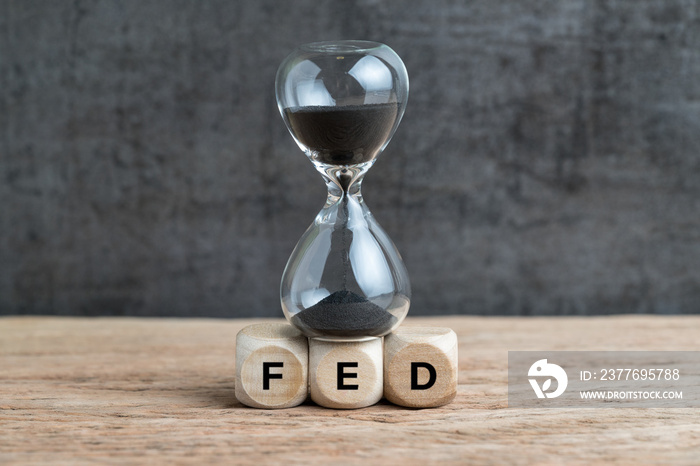 Federal Reserve, FED target and speed to raise interest rate concept, hourglass or sandglass on cube wooden block with alphabet building acronym FED on wooden table with dark background