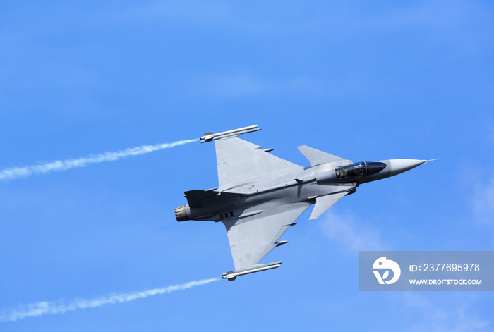 Modern jet fighter flying against a blue sky. White smoke trail.