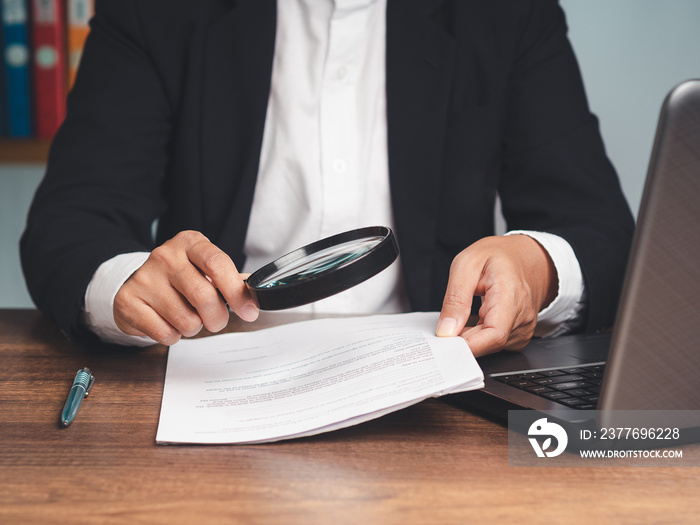 Close-up of a businessman’s hand holding a magnifying glass and looking at reading documents while sitting at the tabl