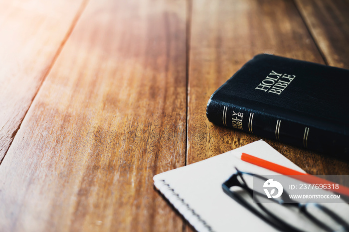 holy bible with eye glasses and note book, pencil on wooden table with window light in the morning, copy space