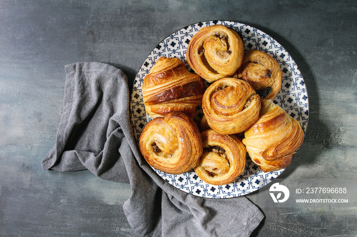 Variety of homemade puff pastry buns cinnamon rolls and croissant served in ceramic plate over blue texture background. Flat lay, space