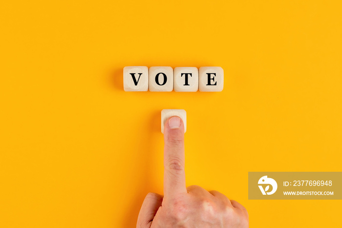 The word vote written on wooden cubes with a male hand pushing the voting button. Online voting concept in politics or business meetings.