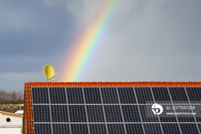 Rainbow over a tiled roof with solar panels. Satellite dish with a smile .