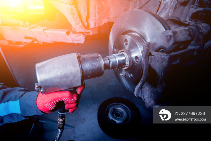 Professional car mechanic working with pneumatic wrench in auto repair service.