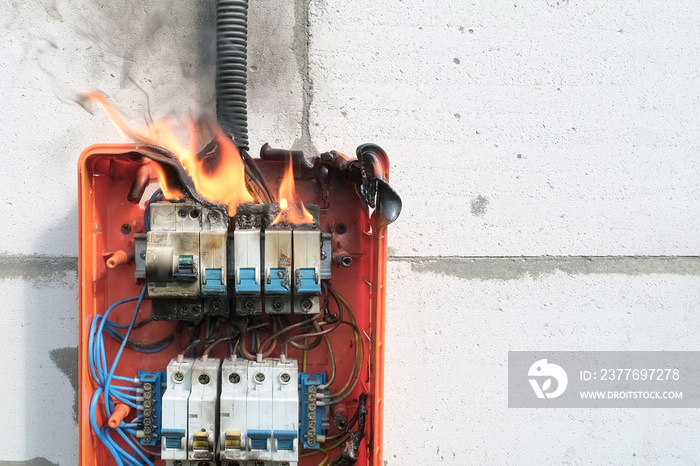 Burning switchboard from overload or short circuit on wall. Circuit breakers on fire and smoke from overheating due to poor connection. Dangerous home electrical wiring concept, copy space