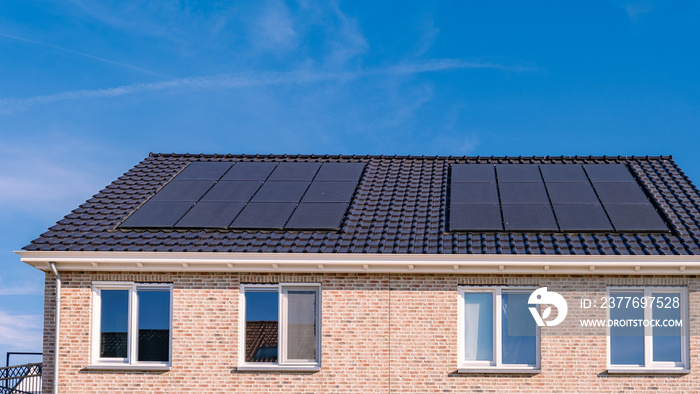 Newly build houses with solar panels attached on the roof against a sunny sky Close up of new building with black solar panels. Zonnepanelen, Zonne energie, Translation: Solar panel, , Sun Energy.