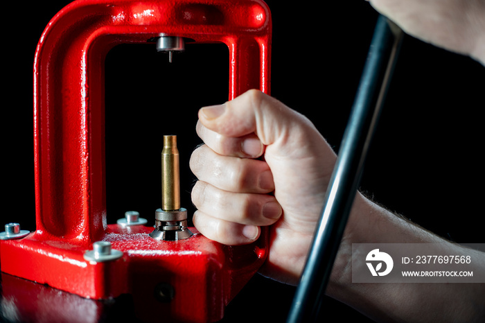 Red hand press and ammo shell against dark background, soft focus. Copy space. The process of making a rifle cartridge