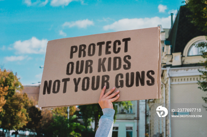 The phrase   Protect our kids not your guns   on a carton banner in men’s hand. Human holds a cardboard with an inscription. Gun violence. Law. USA. Ban