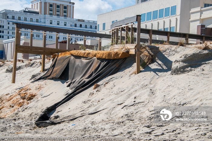 Erosion of the sand of the beach with destruction of a asphalt path after a hurricane and storm. There are large buildings in the background