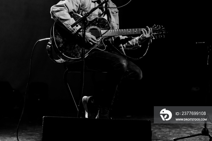 Male musician playing guitar on stage. Black and white high contrast. Pop singer doing a live, instrumental, acoustic concert. Unrecognizable person. Grunge concept. Black background