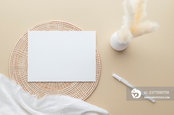 White invitation card, Blank Paper mockup on a beige background,  reeds grass in a vase, white blanket, Rattan basket, Flat lay, top view, copy space