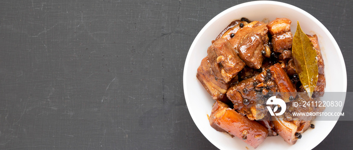 Homemade Filipino Adobo Pork in a white bowl on a black surface, top view. Flat lay, overhead, from above. Space for text.