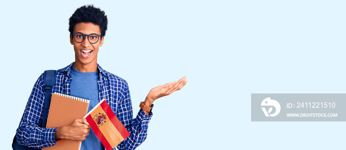 Young african american man wearing student backpack holding spanish flag celebrating victory with happy smile and winner expression with raised hands