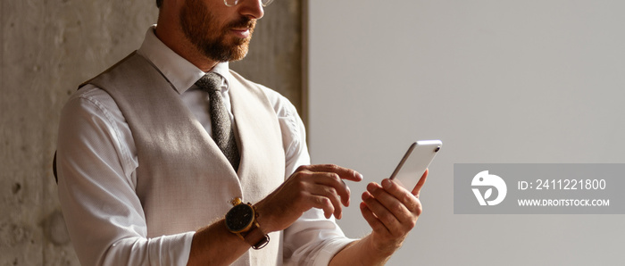 Banner crop of businessman in vest and shirt using mobile phone in modern office, banner