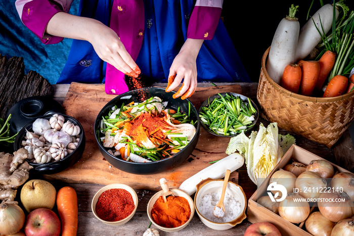 Korean woman is wearing a traditional hanbok, she making Kimchi which is a fermented food preservation of Korean people consisting of many fresh vegetables and fruits, to food concept.