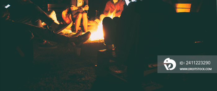 The group of friends are sitting near the bonfire in the night and talking about something