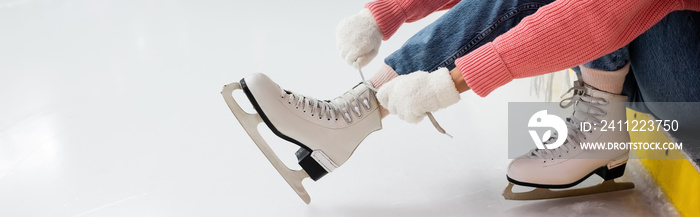 cropped view of woman tying shoe laces on ice skates, banner.