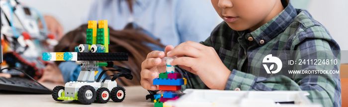 Panoramic crop of schoolboy with building blocks modeling robot in stem school