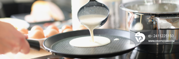 A man fries pancakes in a frying pan at home in the kitchen