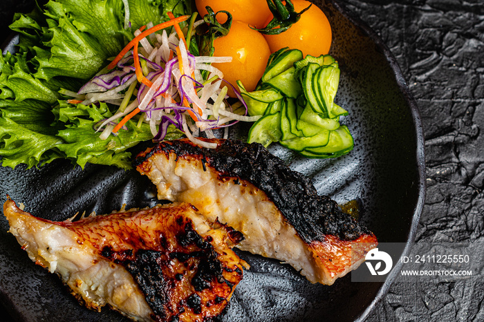 Grilled tilefish marinated with saikyo-miso and tomato salad on a black plate against a black design board.