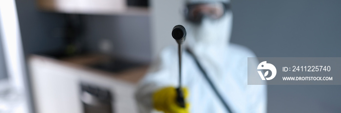 Disinfector in protective suit holding spray with liquid to kill insects closeup