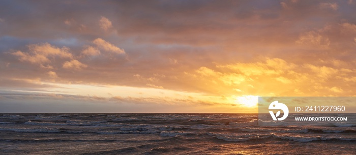 Baltic sea after the storm at sunset. Dramatic sky, glowing clouds, dofty golden sunlight, waves, splashing water. Picturesque panoramic scenery. Nature, environment, ecology