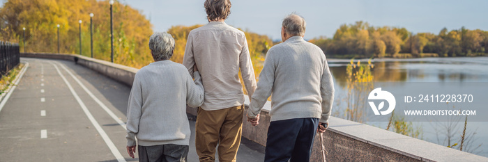 An elderly couple walks in the park with a male assistant or adult grandson. Caring for the elderly, volunteering BANNER, LONG FORMAT