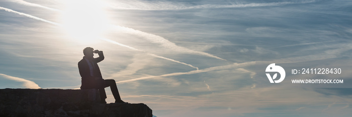 Wide panorama view of businessman in a suit sitting on a wall