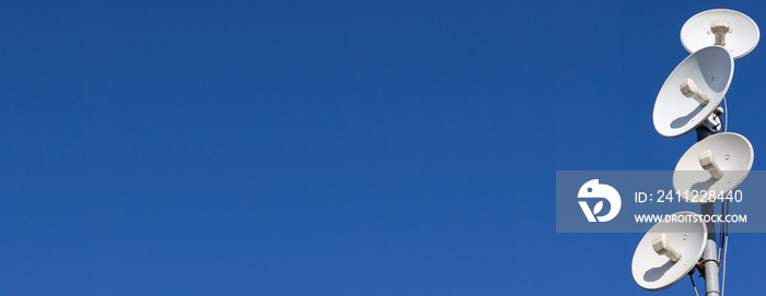 Several telecommunications antennas of a cellular network and wireless internet against a blue sky. Receiving and digitizing multiple pieces of information at once. Panoramic frame.