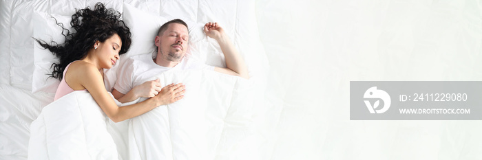 Husband and wife sleep soundly under a white blanket. A man sleeps on his back, and a woman on his side