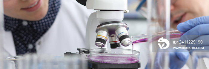 Close-up view of biochemist adding bright violet substance in glass container. Female chemist in glassware going to examine sample through microscope. Lab concept