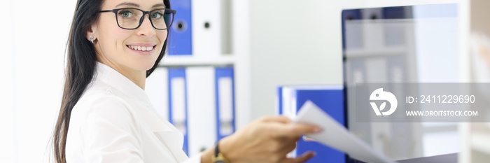 Smiling portrait of secretary who is holding papers next to the printer. Office vacancies without work experience concept