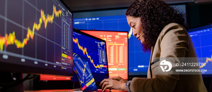 Female Asian successful professional broker trader investor typing on laptop computer studying graph chart analysis value growth report when buy sell trade stock transaction online in trading room