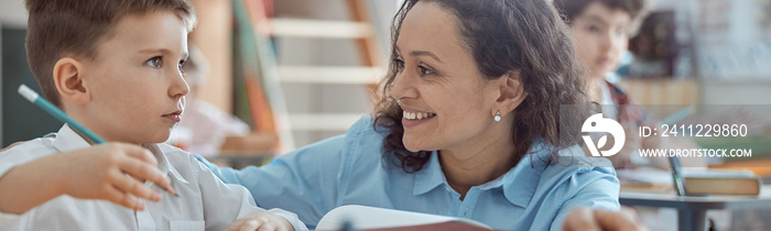 Happy kind teacher is helping kids in elementary school lessons.