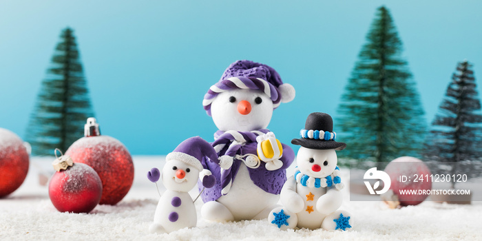 Funny toy snowmen and red Christmas balls in a decorative forest on artificial snow