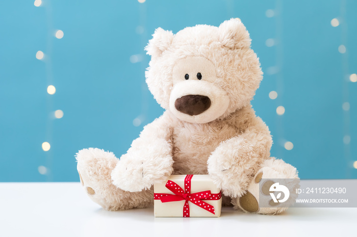 A teddy bear and gift box on a shiny light blue background