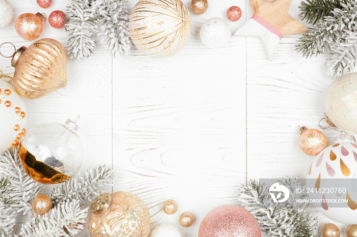 Christmas frame of snowy branches and dusty rose, gold, and white ornaments. Top view on a white woo