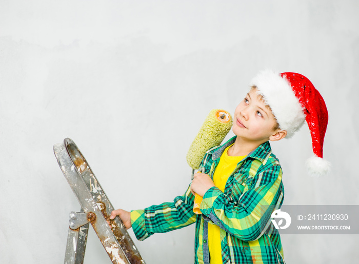 Pensive boy in a red christmas hat holding roller for painting