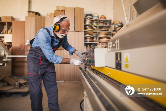 Side view of a senior carpenter using an edgebanding machine