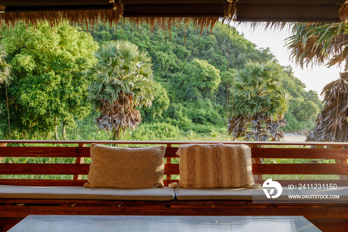 Cozy and comfortable wooden sofa and textile pillows with a scenery of tropical forest atmosphere an