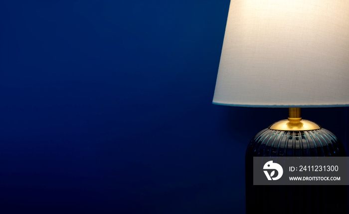 Close-up luxury table lamp with white fabric, blue glass, and gold color materials shining on dark b