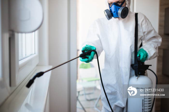 Exterminator in work wear spraying pesticide with sprayer