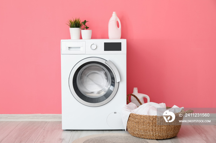 Modern washing machine with laundry near color wall