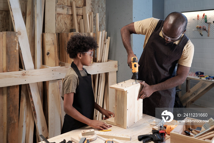 Waist up portrait of African-American father and son working in carpentry workshop together and buil